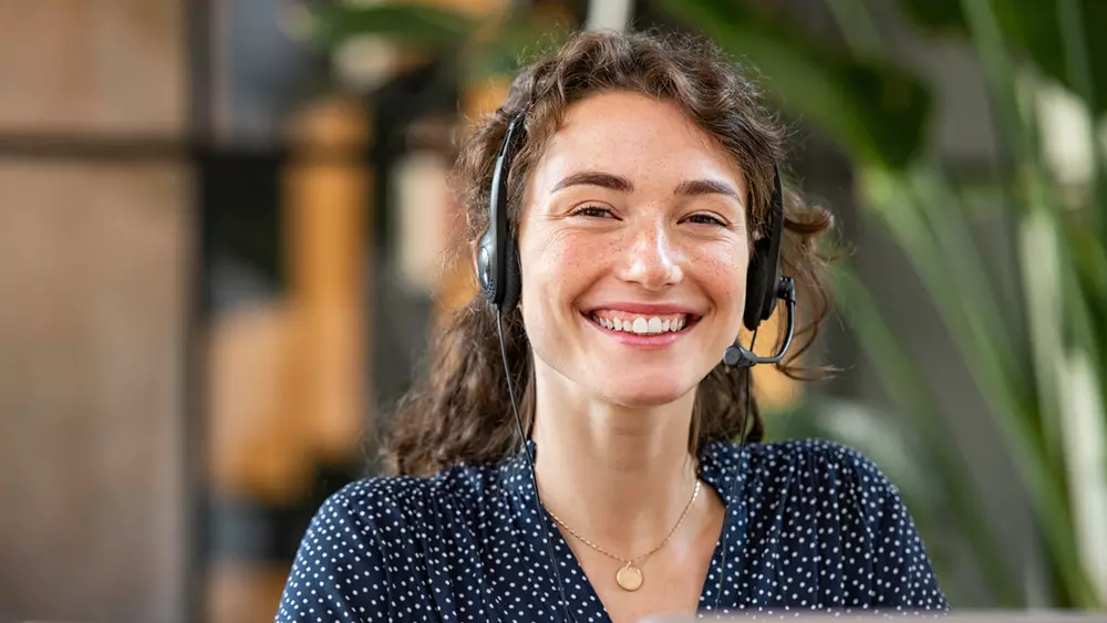 En kvinlig kundtjänstmedarbetare ler in mot kameran. 