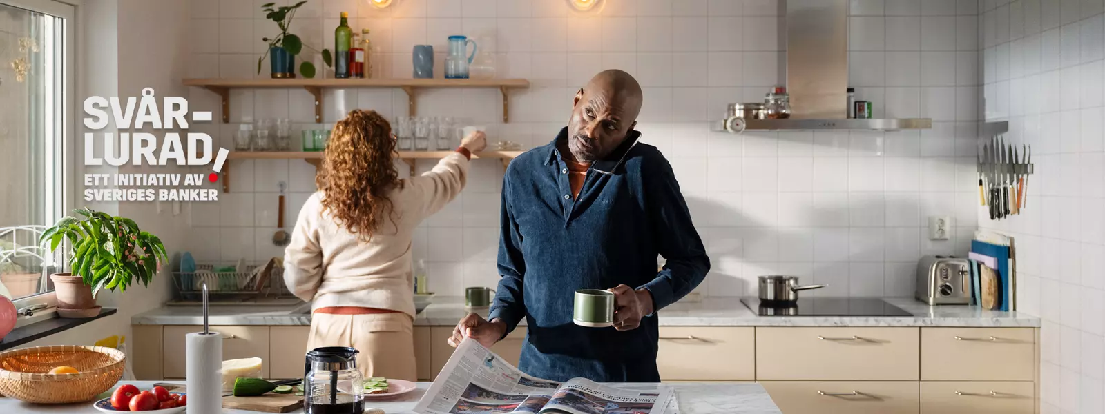 En man läser tidningen, pratar i telefon och dricker kaffe samtidigt.