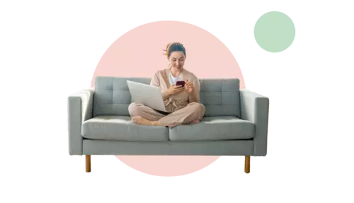 En kvinna sitter hemma i soffan med sin mobil och laptop