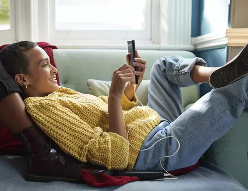 Kvinna ligger i soffa och kollar på sin mobil