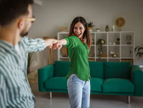En man och en kvinna dansar i ett rum med en soffa i bakgrunden.