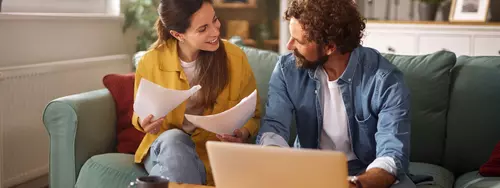 Par sitter i soffan med dator och dokument