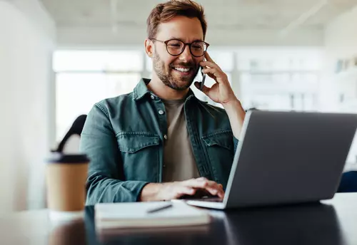 En man pratar i telefonen och kolla på laptopen