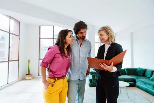 En mäklare står med ett par och visar en broschyr