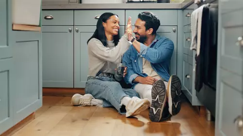 Två personer sitter på golvet i ett kök och gör high five med varandra.