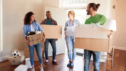 Fyra personer står i ett rum. Ytterdörren bakom är öppen. De bär alla på flyttlådor.