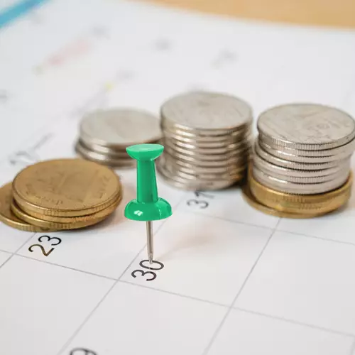 En knappnål som sitter i en almanacka med lite mynt runt om.