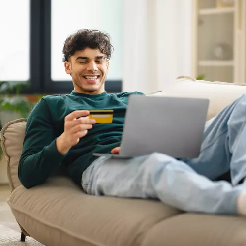 En kille kollar på sitt kreditkort i soffan