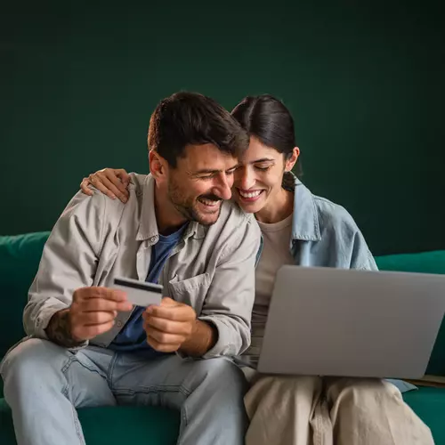 Två personer sitter i soffan med ett kreditkort och dator
