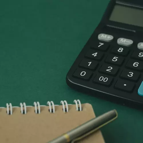 En bild på en miniräknare och ett anteckningsblock med en penna på.