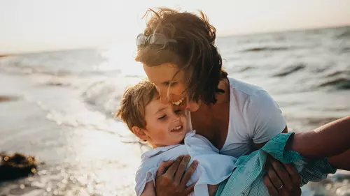 Mamma lyfter sin son på stranden