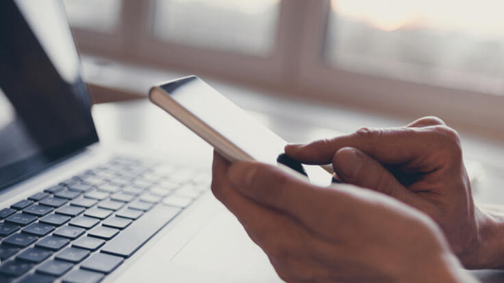 Person sitter vid sin mobil och dator