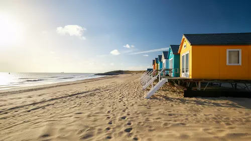 En sandstrand med badhyttar och klarblå himmel 