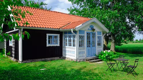 En sommarstuga. Framför sommarstugan står ett litet bord och några stolar. 