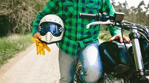 En person står bredvid sin motorcykel med hjälmen under armen