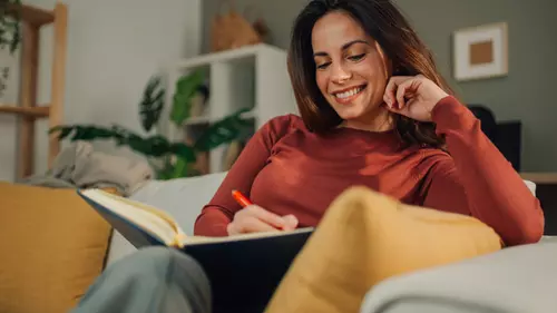 Kvinna sitter i soffan och skriver i ett anteckningsblock