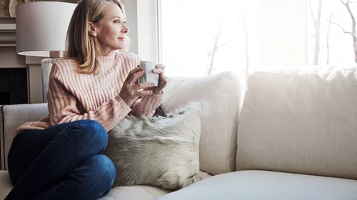 Kvinna dricker kaffe i soffan och tittar ut 