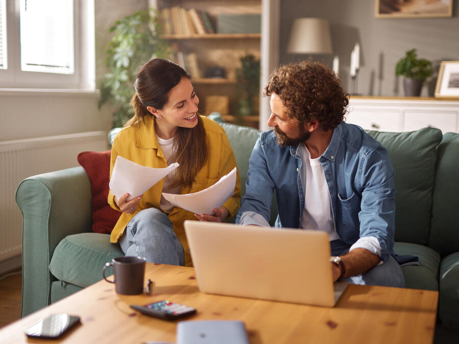 Par sitter i soffan med dator och dokument