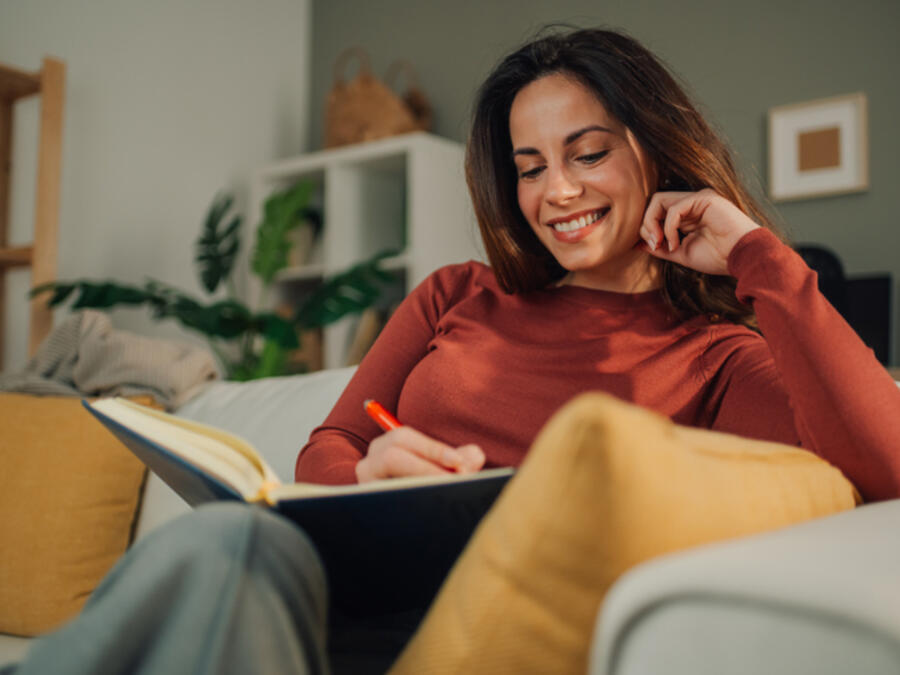 Kvinna sitter i soffan och skriver i ett anteckningsblock
